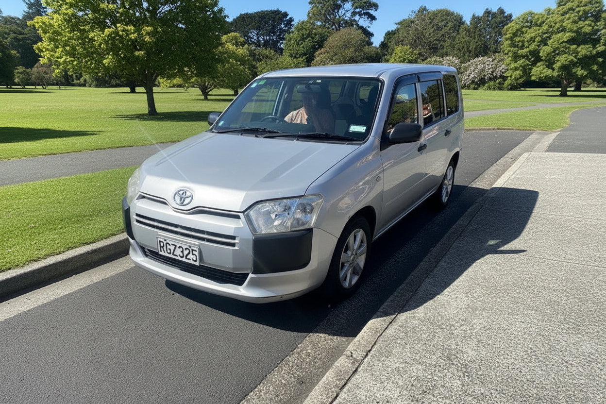 Silver Toyota van parked on a street with buildings in the background
